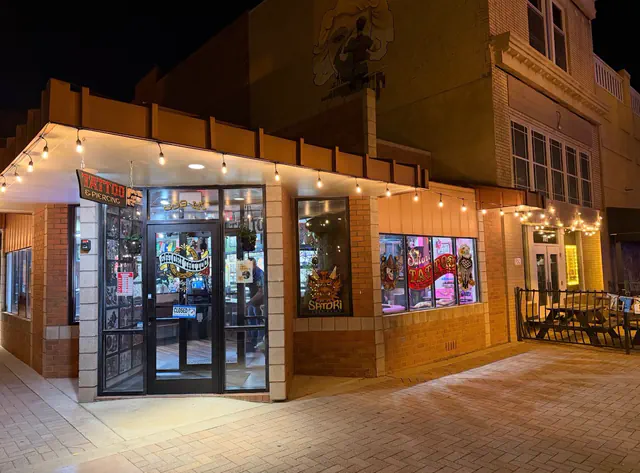 The Satori Tattoo storefront in Greeley at night, with string lights over the corner entrance, a Tattoo and Piercing sign, and the shop's name on the door and windows