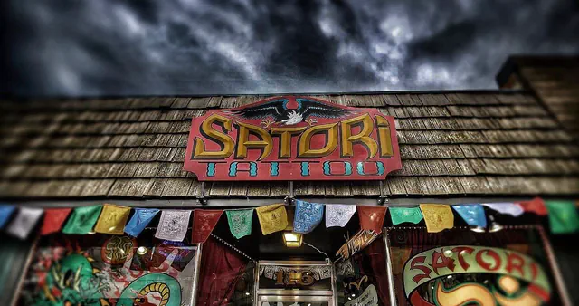 The Satori Tattoo storefront on 4th Street in downtown Loveland, with the painted sign, prayer flags, and the dragon and Om window murals