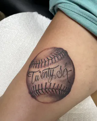 Black and grey baseball tattoo with the words Twenty Six in script across it