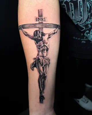 Black and grey realism crucifixion with an INRI sign at the top of the cross, on a forearm