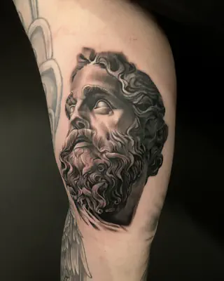 Black and grey realism tattoo of a bearded Greek statue head, on an upper arm