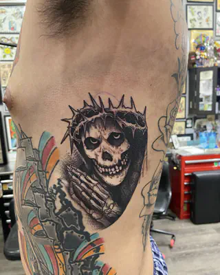 Black and grey hooded skull with a crown of thorns, on the ribs