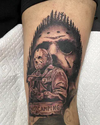 Black and grey horror tattoo of Jason Voorhees in his hockey mask under a pine treeline, with a No Camping banner, on a forearm