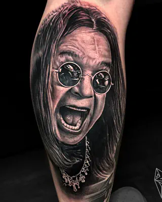 Black and grey realism portrait of Ozzy Osbourne in round sunglasses, mouth open mid-scream, on a forearm