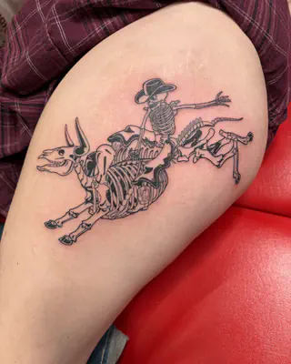 Black and grey line work skeleton cowboy riding a bucking skeleton bull, on a thigh