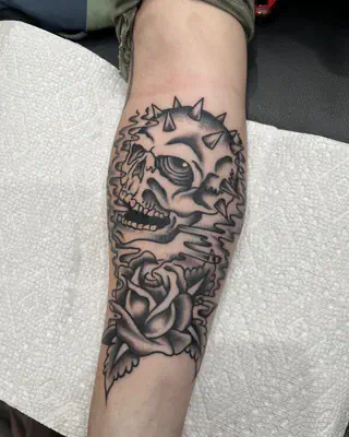 Black and grey skull with spikes above a shaded rose, on a forearm
