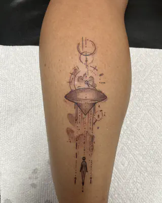 Fine line tattoo of a UFO beaming light down over a small figure, with moon symbols above, on a calf