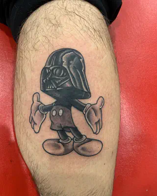 Black and grey tattoo of a cartoon mouse wearing Darth Vader's helmet, on a calf