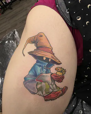 Color tattoo of a little black mage in a tall orange hat holding a yellow bird, on an upper arm
