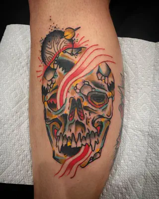 Color tattoo of a cracked skull with a red streak and a ringed planet, on a calf
