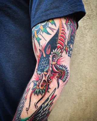 Color tattoo of a blue dragon with pink flames, part of a full arm sleeve