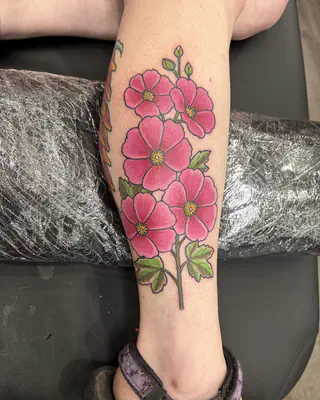 Color tattoo of pink hollyhock flowers on a tall stem, on a calf
