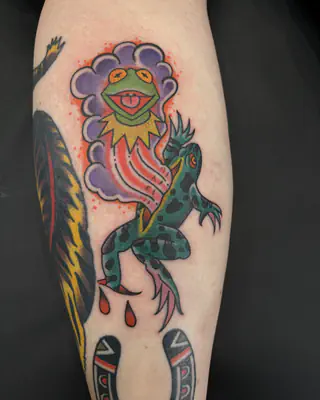 Color tattoo of Kermit the Frog in a purple cloud above a spotted frog and a horseshoe, on a calf