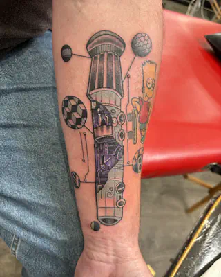 Color tattoo of a lightsaber hilt surrounded by floating orbs, with a small cartoon figure, on a forearm