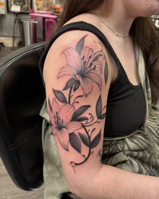 Soft pink and grey lilies blooming across a shoulder and upper arm