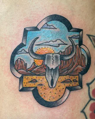 Color traditional tattoo of a steer skull over a desert mesa at sunset, set inside an ornate frame