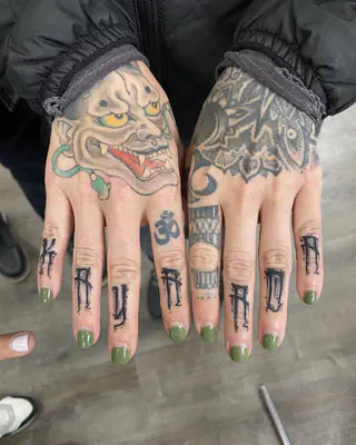 Hand tattoos, a color hannya mask on one hand and ornamental work on the other, with lettering across the fingers