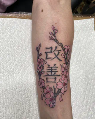 Japanese kanji for kaizen framed by pink cherry blossom branches, on a forearm