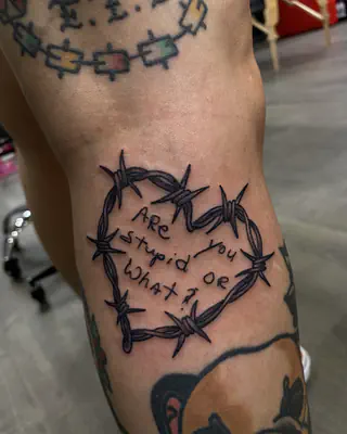 Barbed wire heart framing the handwritten words Are you stupid or what, on a knee