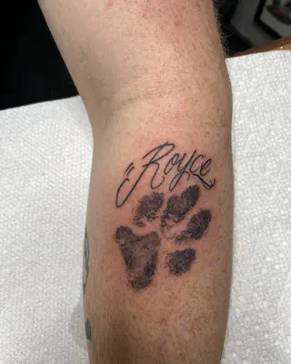 Black paw print with a pet's name in script above it, on a forearm