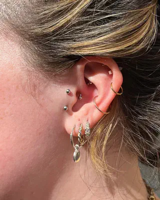Curated ear with helix, tragus, and stacked lobe piercings in silver and gold