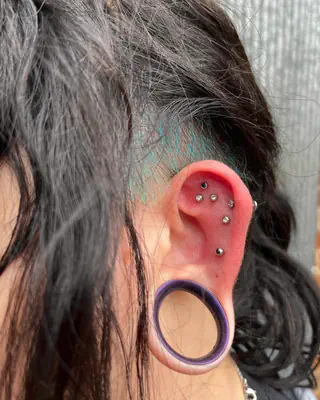 Ear with a row of helix studs and a stretched lobe with a purple-rimmed tunnel