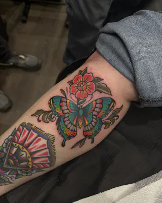 Traditional color butterfly below a red flower, on a forearm