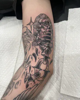 Black and grey traditional tattoo wrapping the elbow, with a brick archway, sparkles, and bold black accents