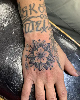 Traditional black and grey flower with dotted rays on the back of a hand