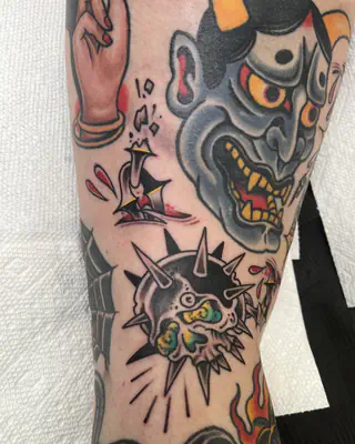 Traditional patchwork on a leg with a blue hannya mask, a spiked ball, and a pointing hand