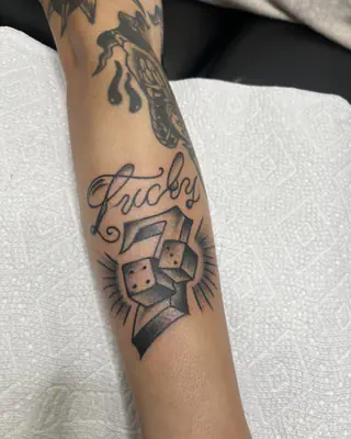 Traditional black and grey dice with Lucky in script above them, on a forearm