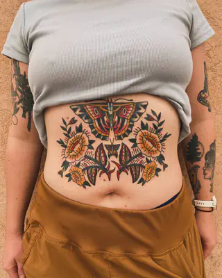 American traditional tattoo across the stomach of a moth over orange flowers and green leaves