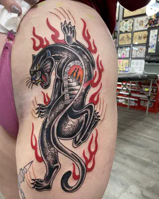 American traditional black panther crawling through red flames, on a thigh