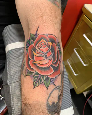Traditional red rose with green leaves, on a forearm