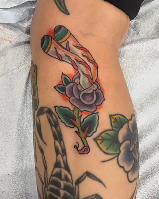 American traditional color tattoo of a purple rose with green leaves beside a black and grey scorpion, on a calf