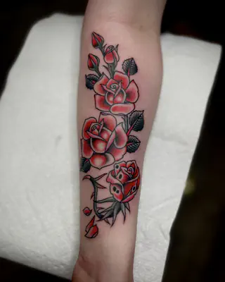 Traditional red roses stacked along a forearm, with green leaves and bold black outlines