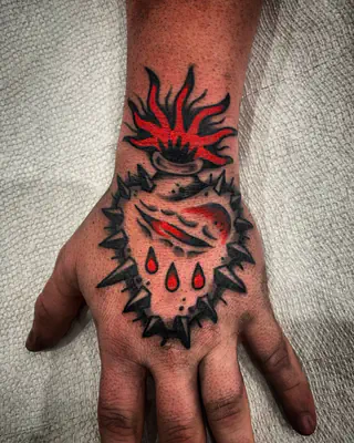 Traditional sacred heart with red flames, a ring of thorns, and blood drops, on the back of a hand
