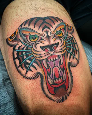 American traditional color tattoo of a snarling tiger head with green eyes, on a thigh