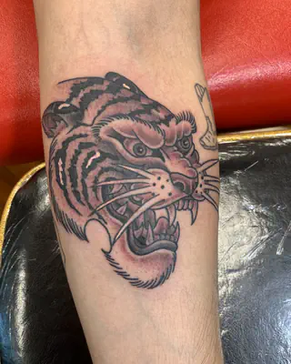 Traditional tiger head with bared fangs in muted color, on a forearm